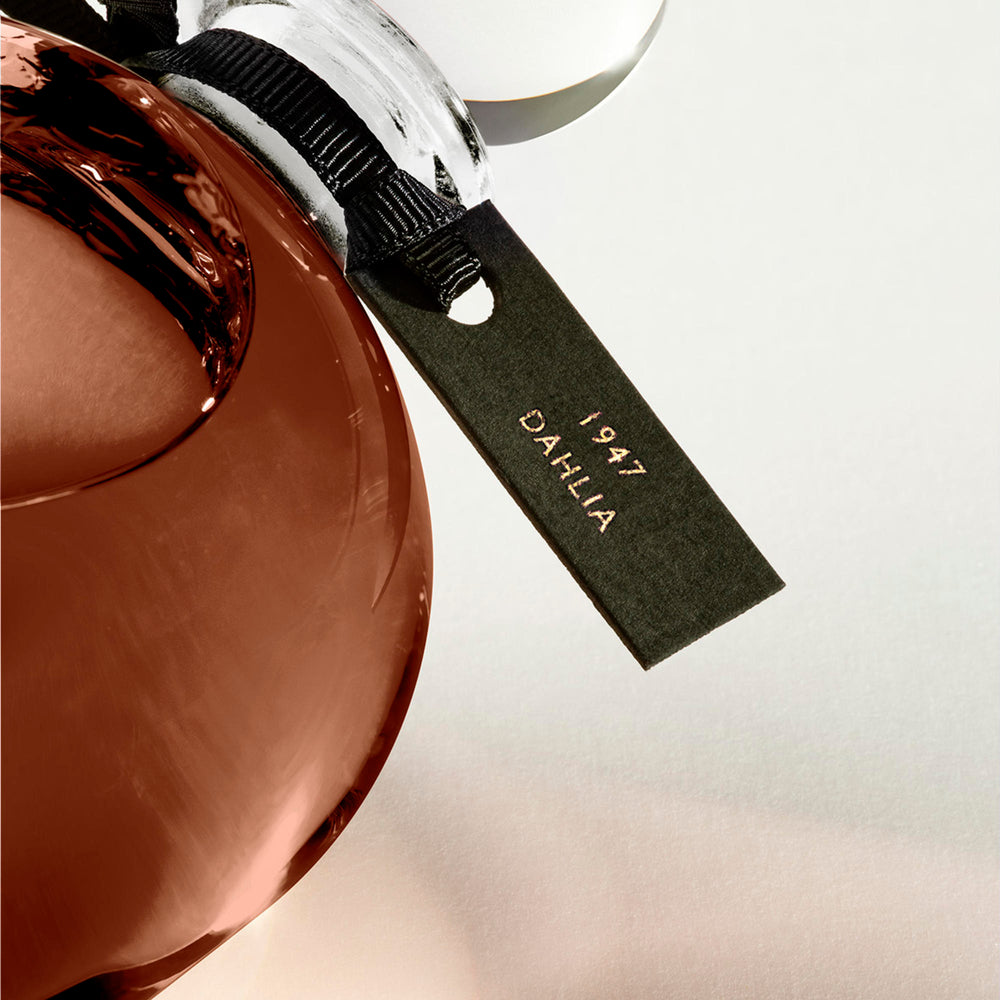 Detail of the top of the 250 ml bottle, with transparent glass and amber perfum. Spherical cap with black ribbon. 1947 Dalhia, a fragrance by Eric Butherbaugh.