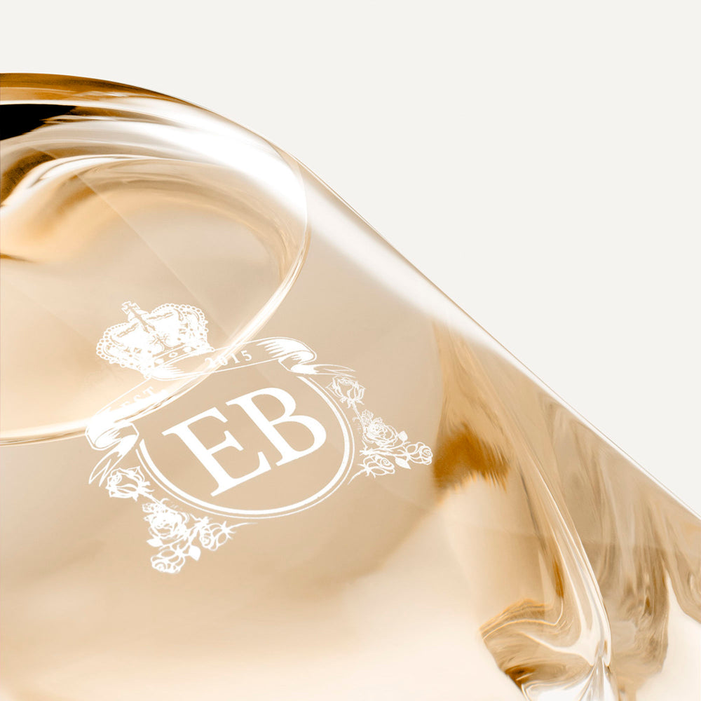 Detail of the bottom of the 250 ml bottle, with transparent glass and orangey perfum. Detail of logo with the EB initials in white ink. Melrose Fresia, a fragrance by Eric Butherbaugh.