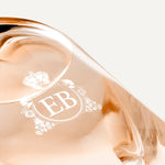 Detail of the bottom of the 250 ml bottle, with transparent glass and orangey perfum. Detail of logo with the EB initials in white ink. Maiden Orange Blossom, a fragrance by Eric Butherbaugh.