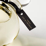 Detail of the top of the 250 ml bottle, with transparent glass and yellowish perfum. Spherical cap with black ribbon. Virgin Lily of the Valley, a fragrance by Eric Butherbaugh.