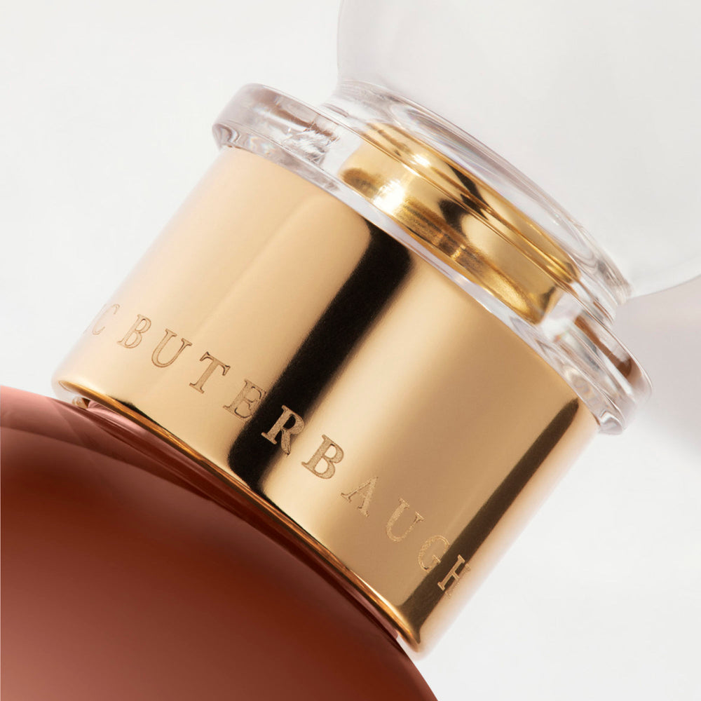 Detail of the top of the 100 ml bottle, with transparent glass and amber perfum. Spherical cap with gold band. 1947 Dalhia, a fragrance by Eric Butherbaugh.