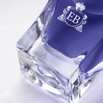 Detail of the bottom of the 100 ml bottle, with transparent glass and violet perfum. Detail of logo with the EB initials in white ink. Fragile Violet, a fragrance by Eric Butherbaugh.