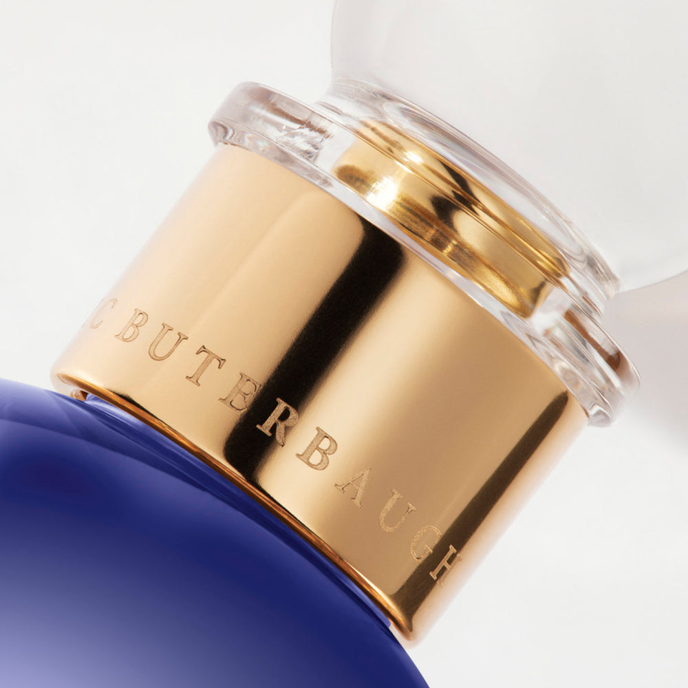 Detail of the top of the 100 ml bottle, with transparent glass and violet perfum. Spherical cap with gold band. Fragile Violet, a fragrance by Eric Butherbaugh.
