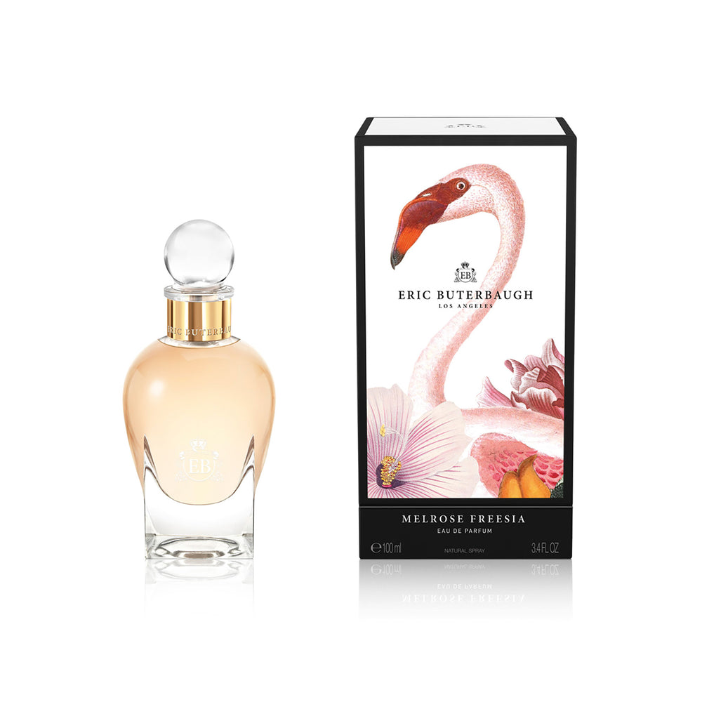 100 ml bottle, with transparent glass and orangey perfum. Spherical cap with gold band. By his side the box, with pink flamingo and flowers illustration, within a black border. Melrose Fresia, a fragrance by Eric Butherbaugh.