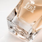 Detail of the bottom of the 100 ml bottle, with transparent glass and orangey perfum. Detail of logo with the EB initials in white ink. Melrose Fresia, a fragrance by Eric Butherbaugh.