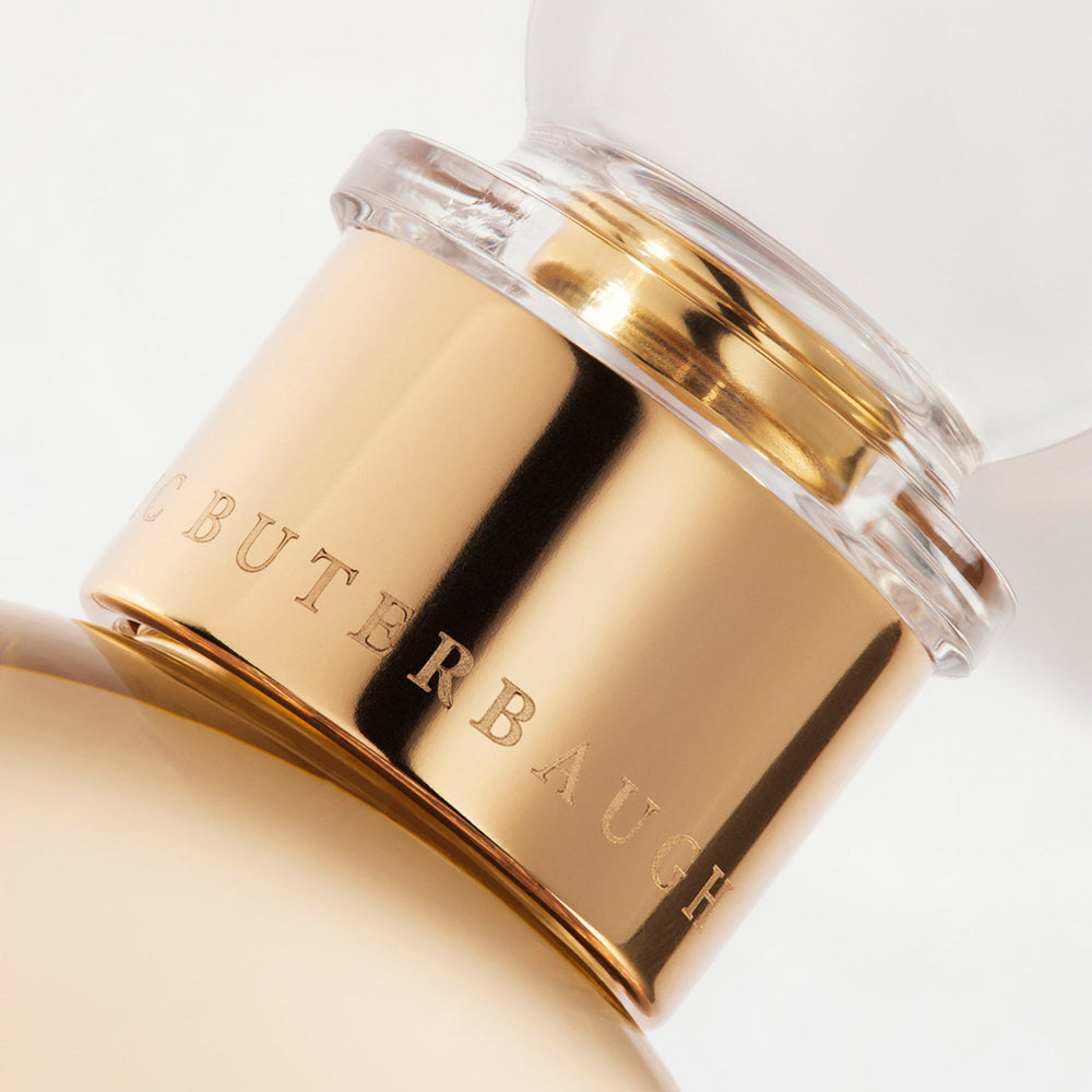Detail of the top of the 100 ml bottle, with transparent glass and orangey perfum. Spherical cap with gold band. Melrose Fresia, a fragrance by Eric Butherbaugh.