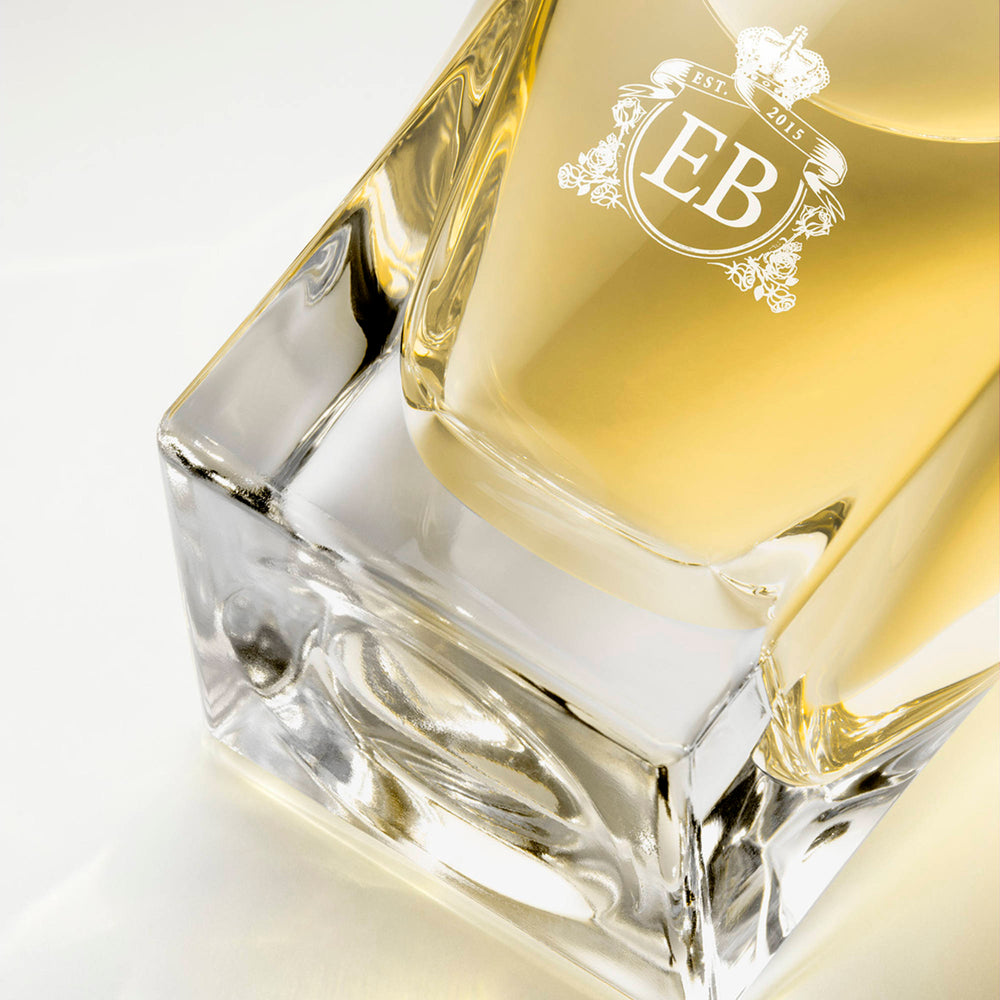 Detail of the bottom of the 100 ml bottle, with transparent glass and yellowish perfum. Detail of logo with the EB initials in white ink. Nick´s Sunflower, a fragrance by Eric Butherbaugh.