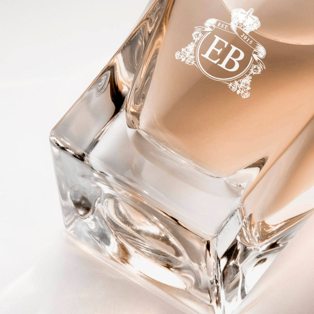 Detail of the bottom of the 100 ml bottle, with transparent glass and orangey perfum. Detail of logo with the EB initials in white ink. Regal Tuberose, a fragrance by Eric Butherbaugh.
