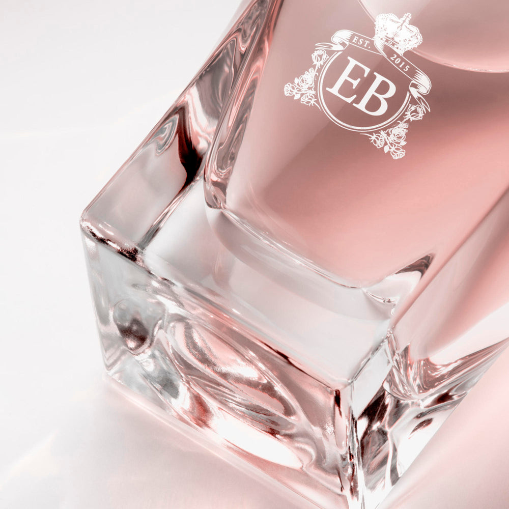 Detail of the bottom of the 100 ml bottle, with transparent glass and pinkish perfum. Detail of logo with the EB initials in white ink. Sultry Rose, a fragrance by Eric Butherbaugh.