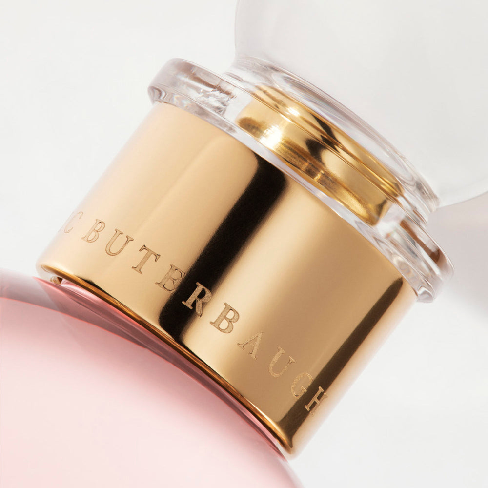Detail of the top of the 100 ml bottle, with transparent glass and pinkish perfum. Spherical cap with gold band. Sultry Rose, a fragrance by Eric Butherbaugh.