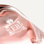 Detail of the bottom of the 250 ml bottle, with transparent glass and pinkish perfum. Detail of logo with the EB initials in white ink. Celestial Jasmine, a fragrance by Eric Butherbaugh.