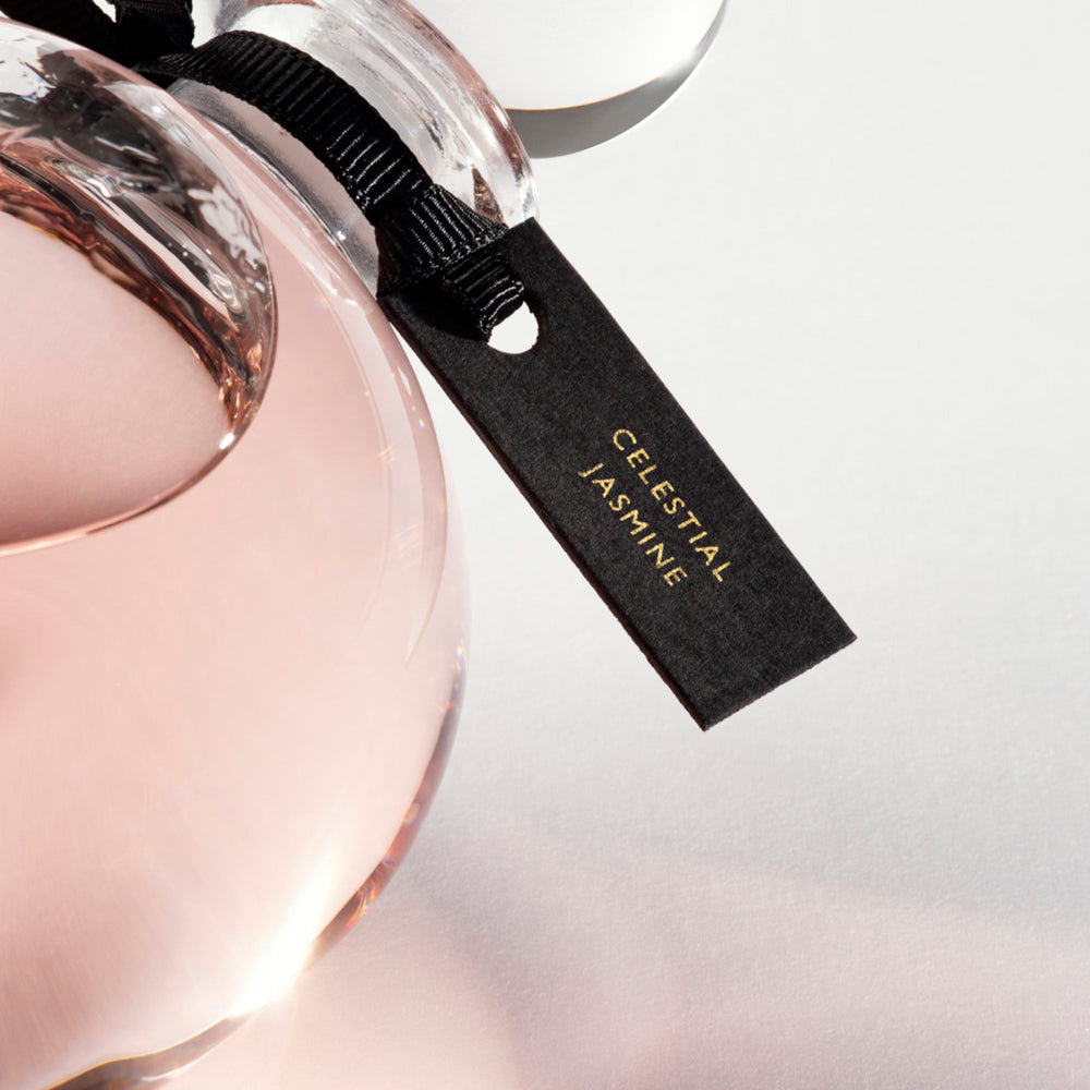 Detail of the top of the 250 ml bottle, with transparent glass and pinkish perfum. Spherical cap with black ribbon. Celestial Jasmine, a fragrance by Eric Butherbaugh.