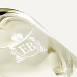Detail of the bottom of the 250 ml bottle, with transparent glass and yellowish perfum. Detail of logo with the EB initials in white ink. Fabulous Magnolia, a fragrance by Eric Butherbaugh.