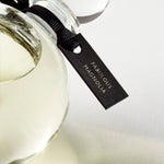 Detail of the top of the 250 ml bottle, with transparent glass and yellowish perfum. Spherical cap with black ribbon. Fabulous Magnolia, a fragrance by Eric Butherbaugh.