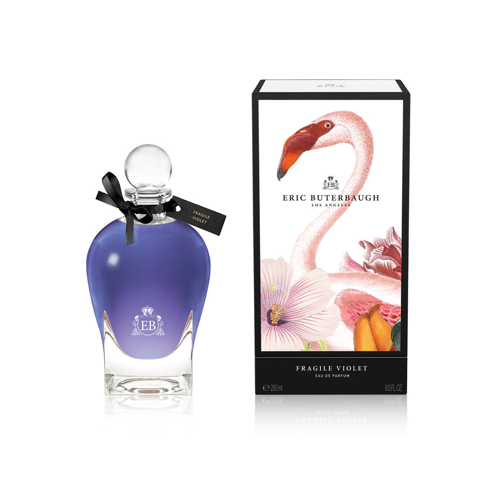 250 ml bottle, with transparent glass and violet perfum. Spherical cap with black ribbon. By his side the box, with pink flamingo and flowers illustration, within a black border. Fragile Violet, a fragrance by Eric Butherbaugh.