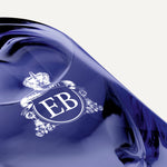 Detail of the bottom of the 250 ml bottle, with transparent glass and violet perfum. Detail of logo with the EB initials in white ink. Fragile Violet, a fragrance by Eric Butherbaugh.