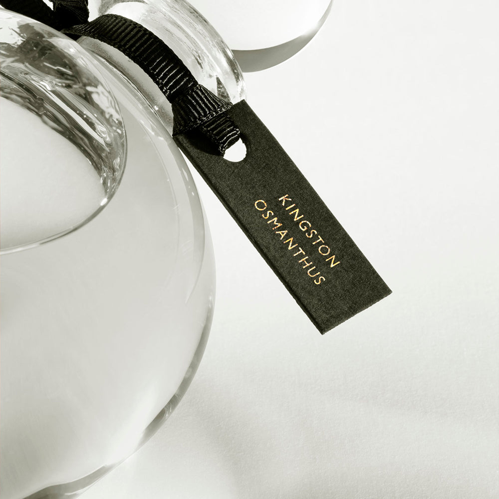Detail of the top of the 250 ml bottle, with transparent glass and yellowish perfum. Spherical cap with black ribbon. Kingston Osmanthus, a fragrance by Eric Butherbaugh.