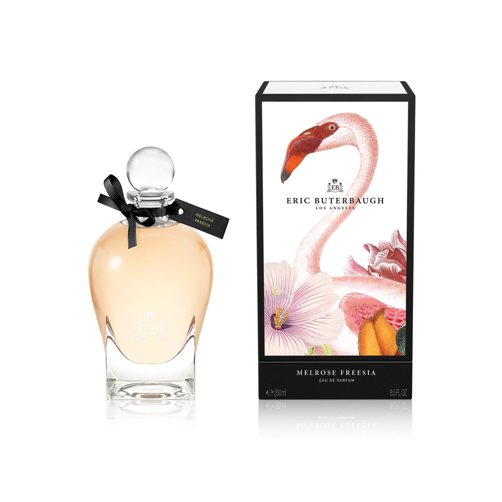 250 ml bottle, with transparent glass and orangey perfum. Spherical cap with black ribbon. By his side the box, with pink flamingo and flowers illustration, within a black border. Melrose Fresia, a fragrance by Eric Butherbaugh.