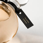 Detail of the top of the 250 ml bottle, with transparent glass and orangey perfum. Spherical cap with black ribbon. Melrose Fresia, a fragrance by Eric Butherbaugh.
