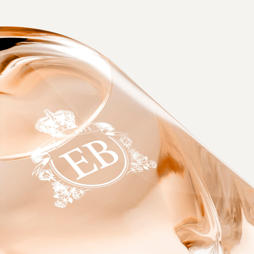 Detail of the bottom of the 250 ml bottle, with transparent glass and orangey perfum. Detail of logo with the EB initials in white ink. Maiden Orange Blossom, a fragrance by Eric Butherbaugh.