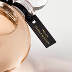 Detail of the top of the 250 ml bottle, with transparent glass and orangey perfum. Spherical cap with black ribbon. Maiden Orange Blossom, a fragrance by Eric Butherbaugh.