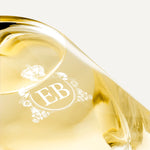 Detail of the bottom of the 250 ml bottle, with transparent glass and yellowish perfum. Detail of logo with the EB initials in white ink. Nick´s Sunflower, a fragrance by Eric Butherbaugh.