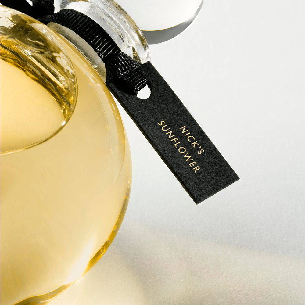 Detail of the top of the 250 ml bottle, with transparent glass and yellowish perfum. Spherical cap with black ribbon. Nick´s Sunflower, a fragrance by Eric Butherbaugh.
