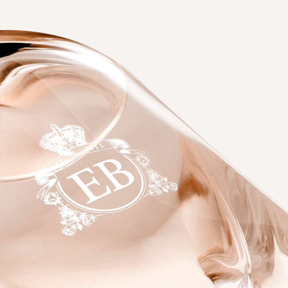 Detail of the bottom of the 250 ml bottle, with transparent glass and orangey perfum. Detail of logo with the EB initials in white ink. Regal Tuberose, a fragrance by Eric Butherbaugh.