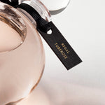 Detail of the top of the 250 ml bottle, with transparent glass and orangey perfum. Spherical cap with black ribbon. Regal Tuberose, a fragrance by Eric Butherbaugh.