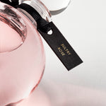 Detail of the top of the 250 ml bottle, with transparent glass and pinkish perfum. Spherical cap with black ribbon. Sultry Rose, a fragrance by Eric Butherbaugh.