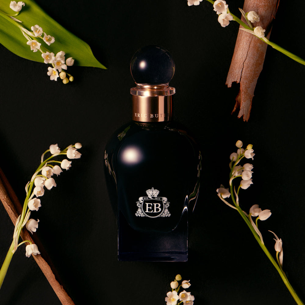 A 100 ml Oud Lily of the Valley bottle lying next to some Lily of the Valley.