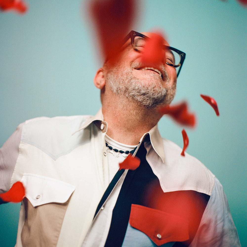 Eric Buterbaugh smiling on blue background at a rain of red rose petals.